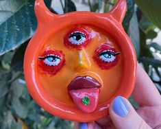 a hand holding an orange ceramic object with eyes and nose painted on it's face