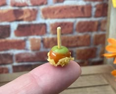 a tiny toy apple sitting on top of a piece of food in someone's finger