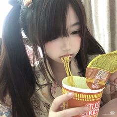 a woman eating noodles from a cup with chopsticks