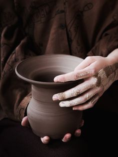 a person holding a clay pot with their hands on the potter's wheel in front of them