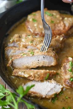 someone is holding a fork over some meat and gravy in a skillet