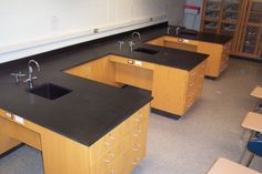 an empty classroom with black counter tops and wooden cabinets on the floor, in front of two rows of desks