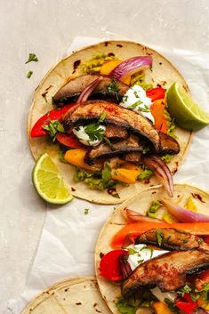 three fish tacos with peppers, onions, and limes on white parchment paper