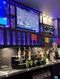 a bar with lots of bottles and liquors on the counter in front of large television screens