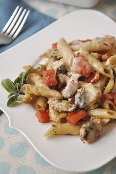 a white plate topped with pasta covered in meat and veggies next to a fork