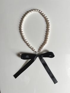 a necklace with pearls and a black ribbon on a white surface, tied in a bow