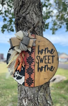 a wooden sign that says home sweet home hanging on a tree in front of a house