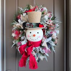 a wreath with a snowman wearing a top hat and scarf hanging on a door