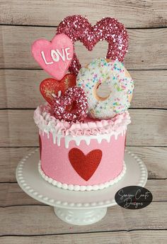 a pink cake topped with donuts and sprinkles in the shape of hearts