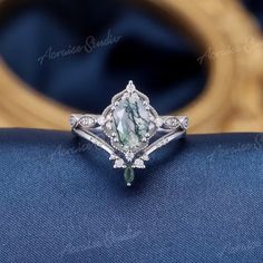 an engagement ring with a green and white stone in the center on a blue cloth