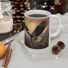 an eagle mug sitting on top of a table next to some pine cones and candles