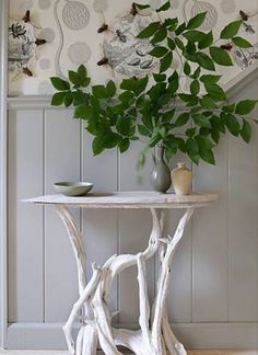 a white table sitting next to a plant in a vase on top of a wooden floor