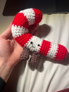 a hand is holding a crocheted red and white object with a stuffed animal