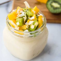 a glass jar filled with fruit salad on top of a white counter next to sliced cucumbers