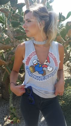 a woman wearing a tank top with an angry bird on the front and back, standing next to a pine tree