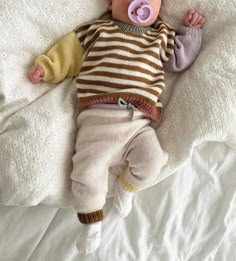 a baby laying on top of a bed with a pacifier in it's mouth