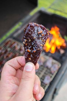 someone holding up a piece of food in front of an open grill with flames on it