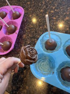 a person holding a chocolate lollipop in front of some cupcakes on a tray