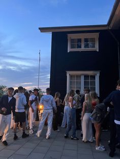 a group of people standing in front of a black house at night with the sun going down