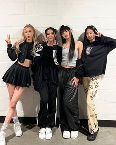 the girls are posing together in front of a wall with their hands up and one is wearing