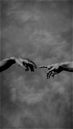 two hands reaching out towards each other in front of a gray sky with white clouds