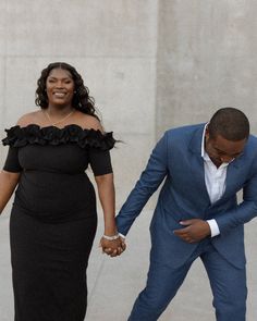 a woman in a black dress and a man in a blue suit are holding hands