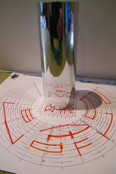 a tall glass sitting on top of a table next to a paper with an orange and red design