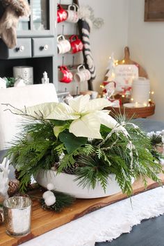 a white bowl filled with greenery on top of a wooden cutting board next to a christmas tree