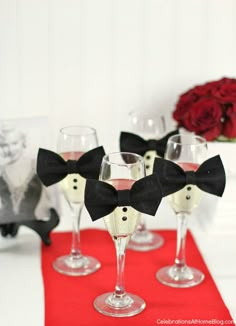 four wine glasses with black bow ties on red place mat and white vases in background