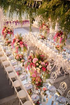 a long table is set with white chairs and pink floral centerpieces on it