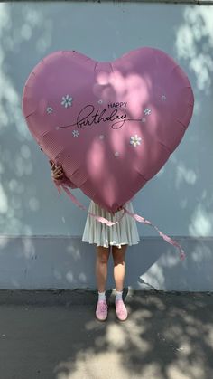 a girl holding a large heart shaped balloon with the words happy birthday written on it