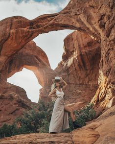 two women standing in front of large rock formations, one wearing a hat and the other holding her leg up