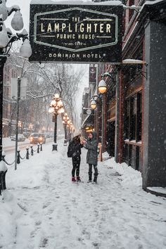 two people walking down a snowy street under a sign for the lamplighter public house