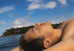 a woman laying on top of a sandy beach next to the ocean under a blue sky