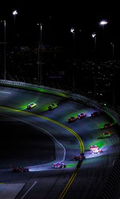 the cars are racing on the track at night time, with bright lights in the background