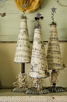 three christmas trees made out of sheet music are sitting on a mantle with a yellow flower