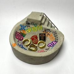 a concrete bowl with some gold scissors and other decorations on it, sitting on a white surface