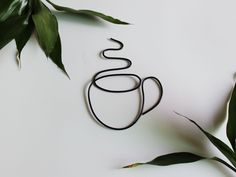 a coffee cup shaped like a snake sitting on top of a white table next to green leaves