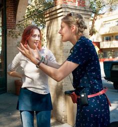 two young women standing next to each other near a building and one is holding her hand out