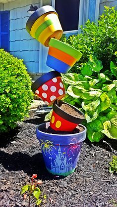 colorful pots are stacked on top of each other in front of some bushes and plants