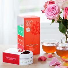 pink roses in a vase next to two tea cups and a carton of tea