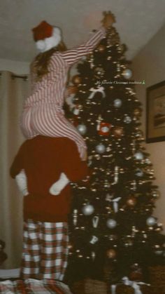 two people standing next to a christmas tree