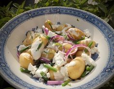 a blue and white bowl filled with food on top of a table next to plants