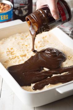 someone pouring chocolate sauce on top of rice in a baking dish with other ingredients nearby