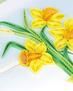 yellow and green paper flowers are on a white surface with two toothpicks in the foreground