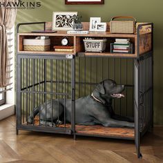 a black dog sitting in a cage next to a table with books and pictures on it