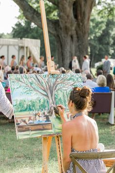 a woman sitting in front of an easel painting a tree with people on it