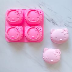 pink hello kitty ice cube molds on a white marble counter top with three pieces cut out to look like cats