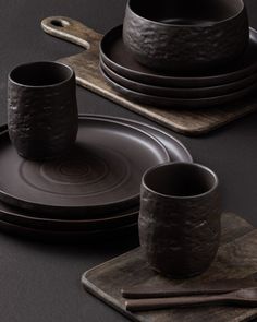 a set of brown dinnerware on a black table with place mats and wooden utensils