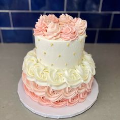 a three tiered cake with pink and white frosting roses on top, sitting on a plate